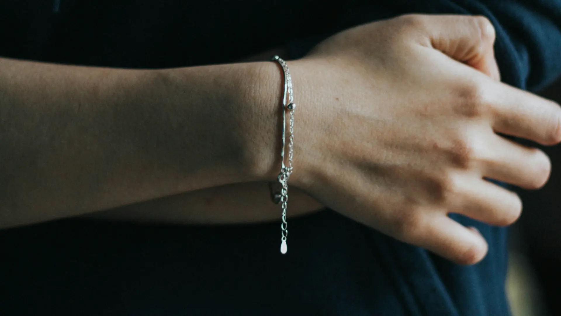 Pulseira de prata destacada no pulso de uma pessoa branca vestindo uma blusa azul escuro.