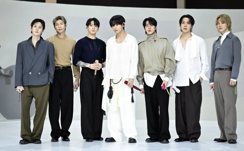 Os sete mebros do BTS posando juntos lado a lado com looks modernos e sofisticados em tons neutros de cinza, bege, branco e preto.