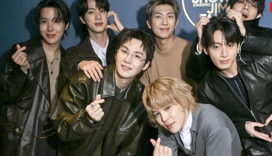 Membros do BTS reunidos usando jaquetas de couro escuras, óculos e anéis em destaque nas mãos enquanto fazem gestos de coração com os dedos.